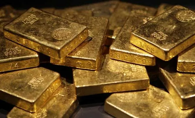 A pile of stamped fine gold bars under low light.