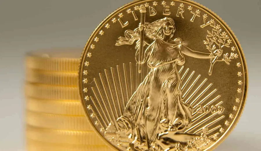 Gold American Eagle coin dated 2009 standing beside a stack of gold coins