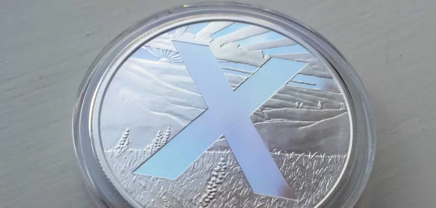 OWNx silver round with a large X over a prairie scene, sealed in a clear capsule