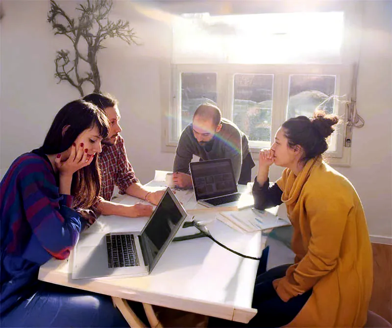 Four colleagues around a white table with laptops and papers, in a sunlit room