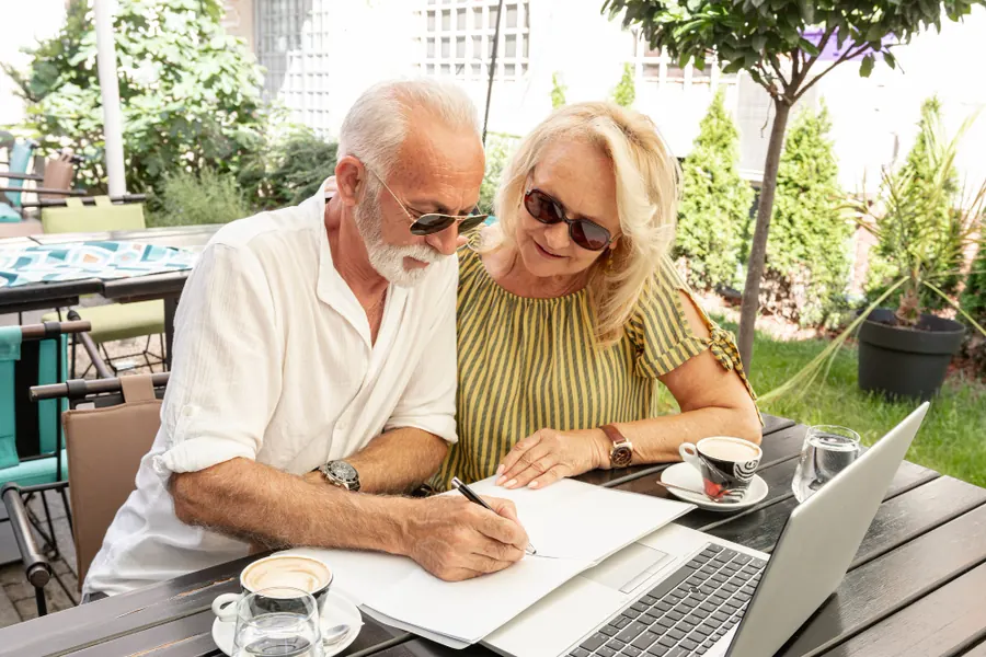 Older couple at a garden table filling in paperwork together next to a laptop