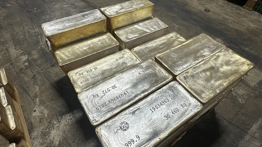Large cast silver bars stamped with serial numbers and weights in kilograms, stacked on a depository floor