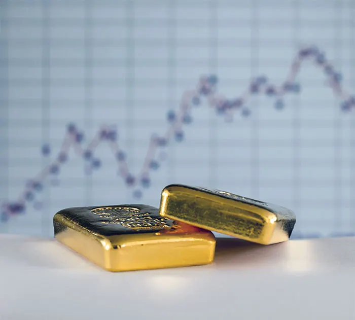 Two small gold bars in front of a blurred price chart